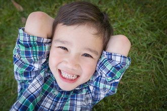 mixed-race chinese and caucasian young boy relaxing on his back outside on the grass