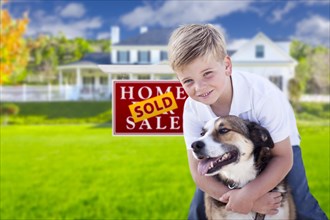 Happy young boy and his dog in front of sold for sale real estate sign and house