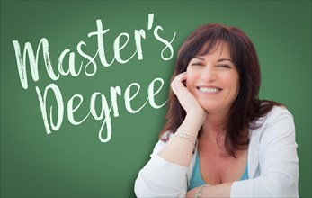 Master's degree written on green chalkboard behind smiling middle aged woman