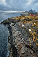 Clif with traditional red rorbu house on Litl-Toppoya islet on Lofoten Islands