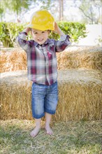 Cute young mixed-race boy laughing with hard hat outside near hay bale