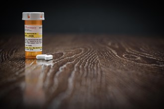 Non-Proprietary prescription medicine bottle and pills on reflective wooden surface