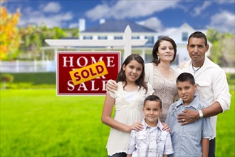 Happy hispanic family in front of their new house and sold home for sale real estate sign