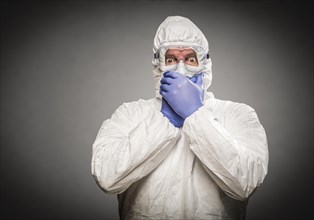 Man covering mouth with hands wearing HAZMAT protective clothing against A gray background