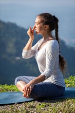 Woman practices pranayama yoga breath control in lotus pose padmasana outdoors in Himalayas in the morning on sunrise. Himachal Pradesh