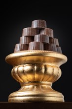 Stack of fine chocolates on golden pillar dish with dark background