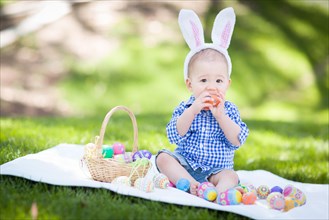 mixed-race chinese and caucasian baby boy outside wearing rabbit ears playing with easter eggs