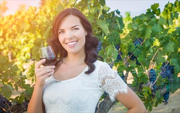 Beautiful young adult woman enjoying glass of wine tasting in the vineyard