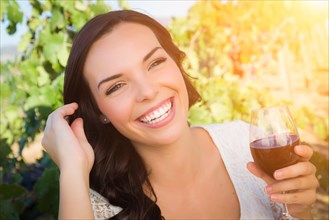 Beautiful young adult woman enjoying glass of wine tasting in the vineyard
