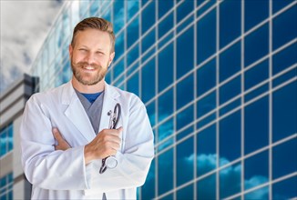 Handsome young adult male doctor with beard in front of hospital building