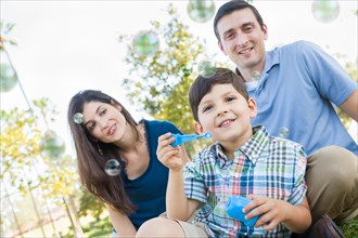 Young boy blowing bubbles with his parents in the park
