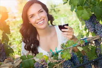 Beautiful young adult woman enjoying glass of wine tasting in the vineyard