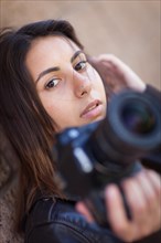 Young adult ethnic female photographer against wall holding camera