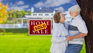 Sold real estate sign with happy affectionate senior couple hugging in front of house
