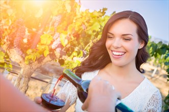 Beautiful young adult woman enjoying glass of wine tasting pour in the vineyard with friends
