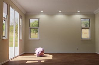 3D illustration piggy bank sitting on the floor of empty room of house with blank wall