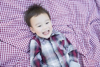 Cute young mixed-race boy laughing on picnic blanket outside