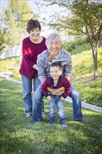 Happy chinese grandparents having fun with their mixed-race grandson outside