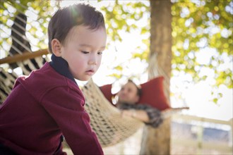 mixed-race boy having fun outside while parent watches from behind in a hammock