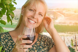 Beautiful young adult woman enjoying glass of wine tasting in the vineyard