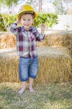 Cute young mixed-race boy laughing with hard hat outside near hay bale