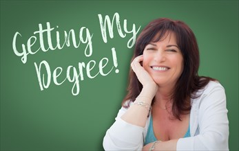 Getting my degree written on green chalkboard behind smiling middle aged woman