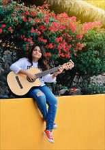 A girl sitting playing guitar outdoors