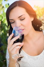 Beautiful young adult woman enjoying glass of wine tasting in the vineyard