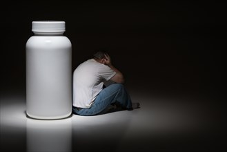 Man holding head sitting next to blank medication bottle