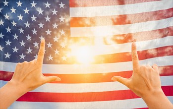Hands framing sun shining through american flag