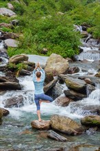 Woman in Hatha yoga balance yoga asana Vrikshasana tree pose at waterfall outdoors