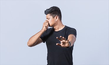 Confused unhappy man grabbing nose with fingers and stretching hand out feeling disgusted