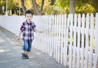Cute young mixed-race boy walking with stick along white fence