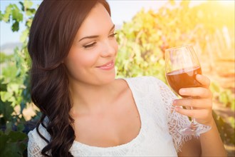 Beautiful young adult woman enjoying glass of wine tasting in the vineyard