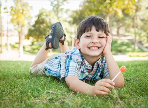 Handsome young boy enjoying his lollipop outdoors on the grass