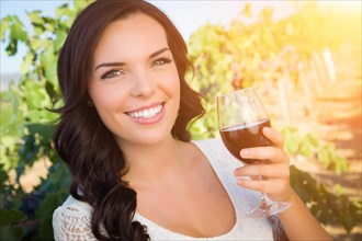 Beautiful young adult woman enjoying glass of wine tasting in the vineyard