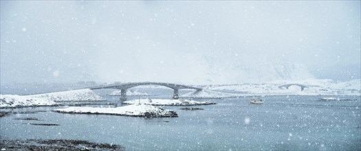 Fredvang bridges in heavy snowfall in winter with fishing ship. Lofoten islands