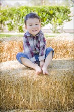 Cute young mixed-race boy having fun on hay bale outside