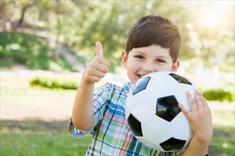 Cute young boy playing with soccer ball and thumbs up outdoors in the park