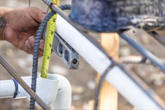 Plumber using level and tape measure while installing PVC pipe at construction site