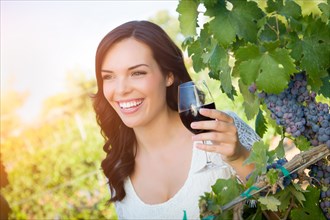 Beautiful young adult woman enjoying glass of wine tasting in the vineyard