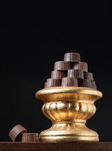 Stack of fine chocolates on golden pillar dish with dark background