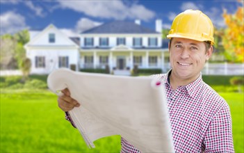 Smiling contractor holding blueprints in front of beautiful custom home