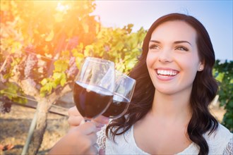 Beautiful young adult woman enjoying glass of wine tasting toast in the vineyard with friends