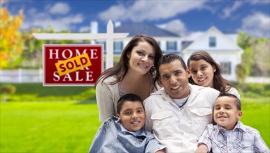 Happy hispanic family in front of their new house and sold home for sale real estate sign