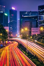 Street traffic in Hong Kong at night. Office skyscraper buildings and busy traffic on highway road with blurred cars light trails. Hong Kong