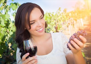 Beautiful young adult woman enjoying glass of wine tasting walking in the vineyard