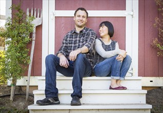 Happy mixed-race couple relaxing on the steps of their barn