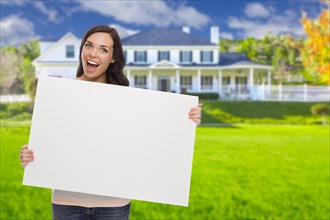 Excited mixed-race female with blank sign in front of beautiful house