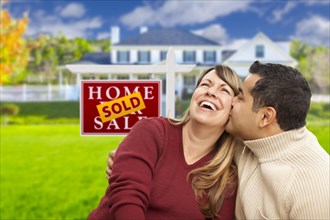 Happy mixed-race couple in front of sold real estate sign